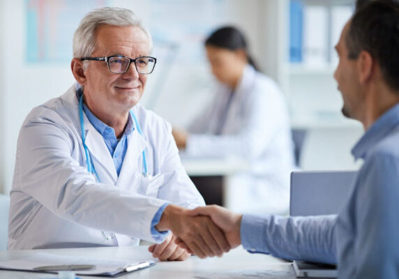 Smiling senior doctor shaking hands to his patient while they sitting at the table at office